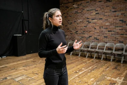 Jeune comédienne en répétition sur une scène de théâtre noir, préparant son audition pour le Cours Florent